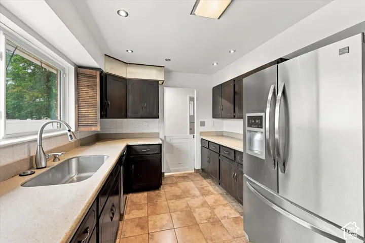 Kitchen featuring dark cabinetry, solid-surface countertops, stainless steel refrigerator, recessed lighting, and tile flooring