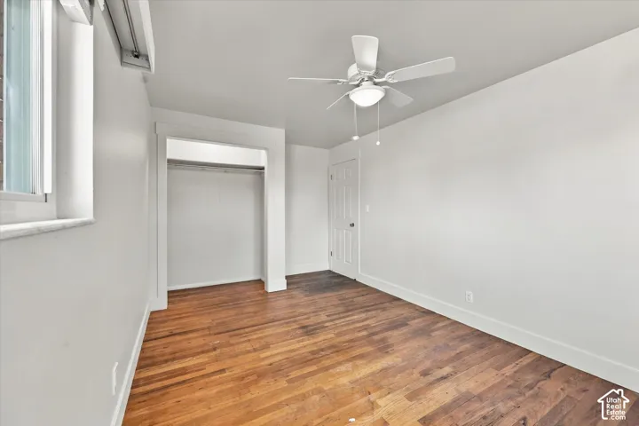 Interior room featuring wood-finish flooring, white walls, a ceiling-mounted fan with integrated lighting, a built-in closet with an arched entryway, and a paneled interior door