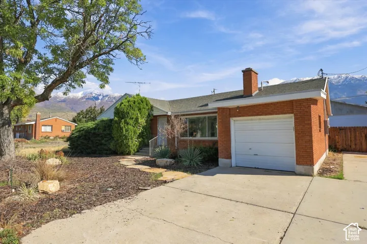 Brick exterior residence featuring an attached garage, concrete driveway, stone walkway, and mountain backdrop