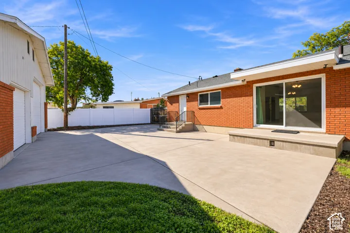 Exterior red brick facade featuring a concrete patio, sliding glass door, detached garage, and white vinyl privacy fencing