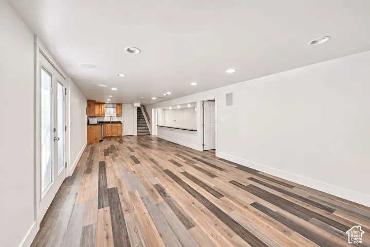 Multi-tone wood-finish flooring, recessed lighting, kitchenette with wood cabinetry, and a built-in refreshment bar featuring a stone-surface countertop