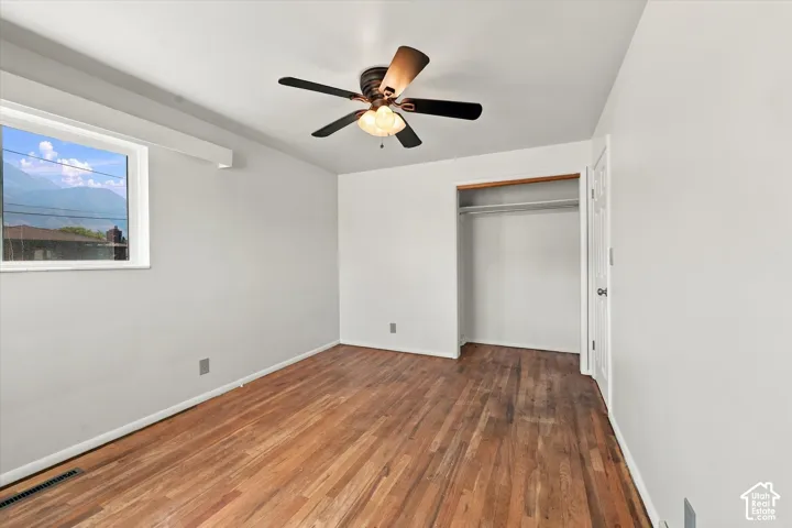 Room featuring wood-finish flooring, a ceiling fan with integrated lighting, a built-in closet with shelving, and a window with mountain scenery