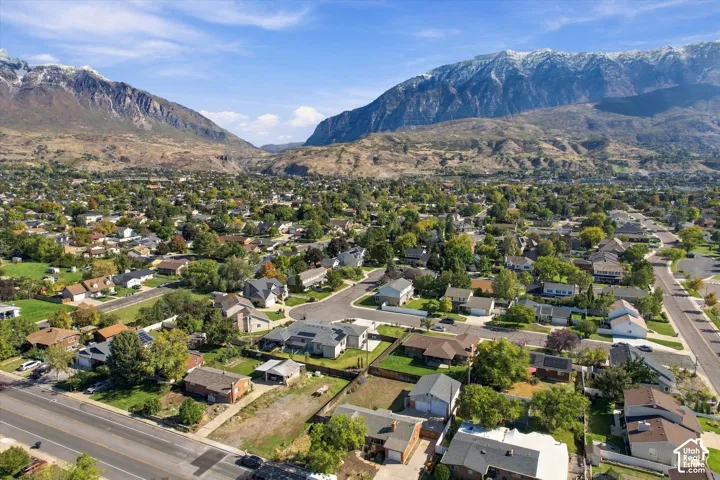 Aerial perspective featuring an established suburban neighborhood with mature tree canopy, asphalt street infrastructure, and a prominent mountain backdrop