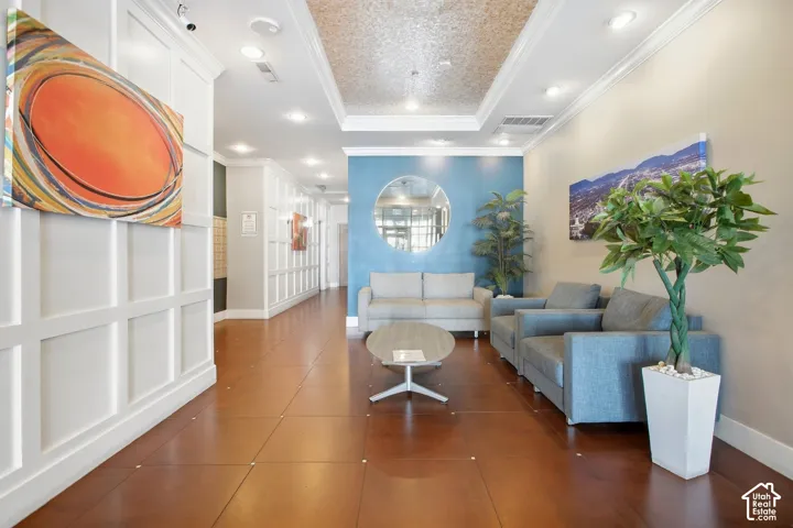 Lobby featuring grid-pattern wall molding, large-format tile flooring with decorative inserts, recessed ceiling lighting, a coffered ceiling with inset textured detailing, and a circular wall-mounted mirror
