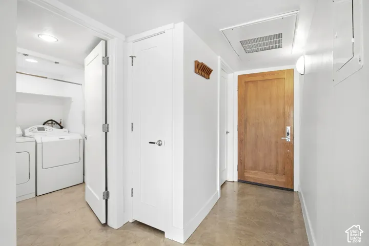 Interior hallway featuring polished concrete flooring, a solid wood entry door with metallic hardware, and white shaker-style interior doors