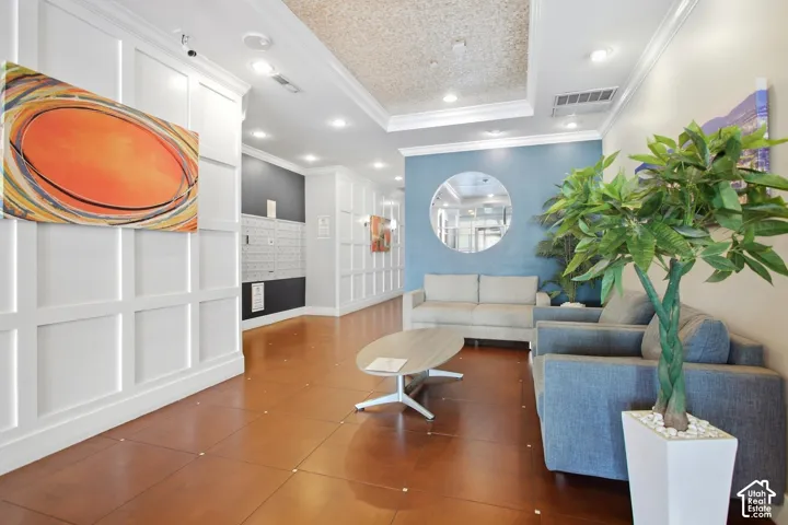 Lobby area featuring grid-patterned wall paneling, large-format tile flooring with decorative inlay, a recessed ceiling with cove lighting, and a circular wall mirror