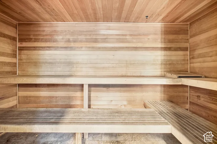 Sauna featuring tongue-and-groove wood paneling, multi-level built-in wood benches, and stone flooring