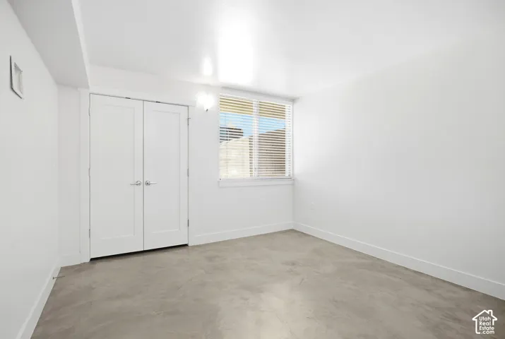 Neutral interior featuring polished concrete flooring, white walls, a single-pane window with horizontal blinds, and double-panel closet doors