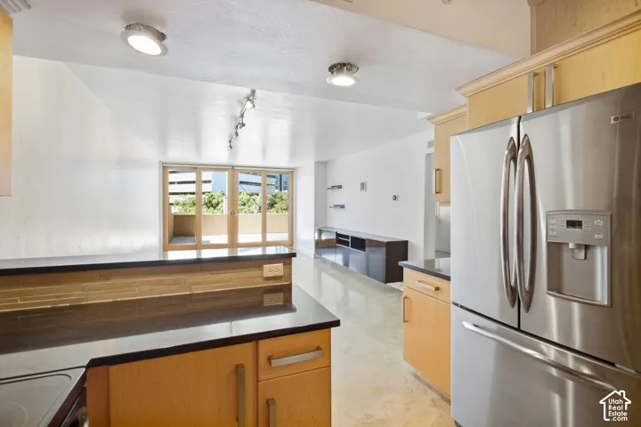 Kitchen featuring light wood cabinetry, dark stone countertops, stainless steel refrigerator, recessed lighting, and sliding glass doors