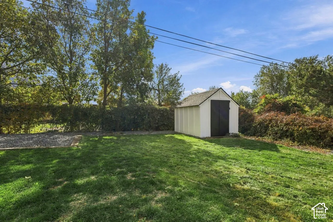 Backyard featuring a detached storage shed with a gabled roof, grass lawn, gravel area, and perimeter hedges