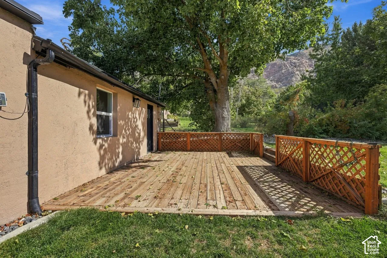 Stucco exterior featuring a wood deck with lattice railings, mature tree canopy, and mountain backdrop