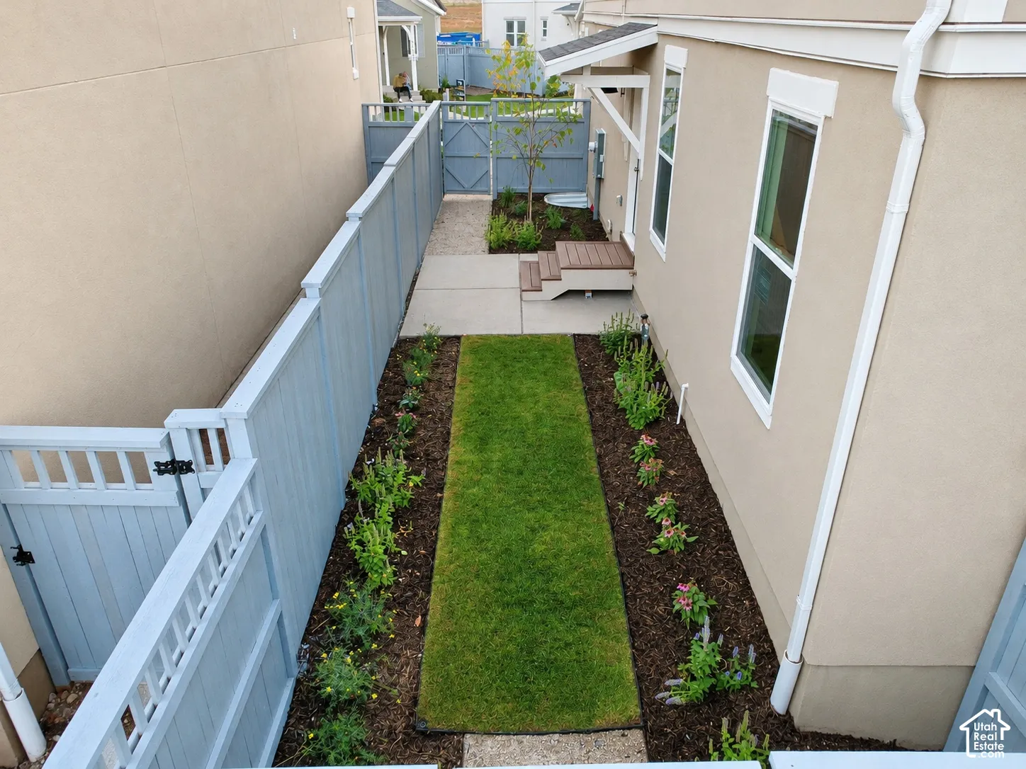 Side yard featuring a manicured lawn, tiered concrete and composite steps, landscape beds with mulch, and a painted wood privacy fence with a gated entry