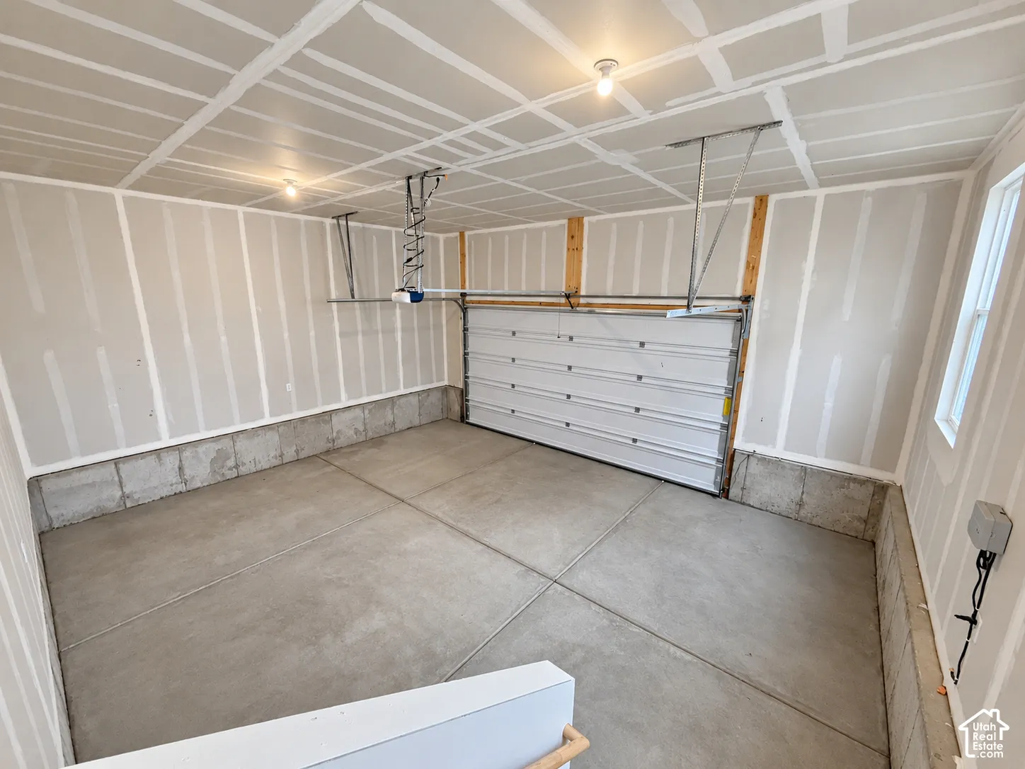Two-car garage featuring a concrete floor, finished drywall, overhead lighting, and an automatic garage door opener