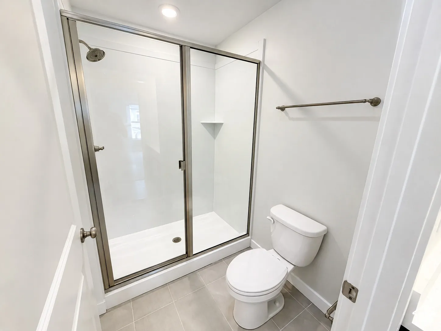 Shower enclosure with a metallic frame, integrated corner shelf, and wall-mounted showerhead, complemented by a floor-mounted toilet and ceramic tile flooring