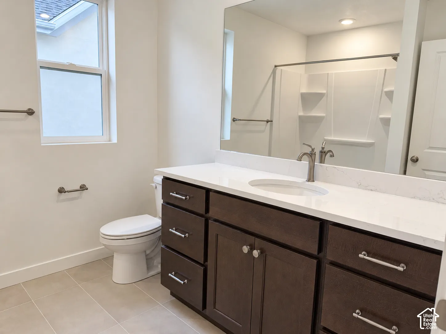 Bathroom featuring dark-stained cabinetry, white stone-composite countertop with an integrated basin, full-width mirror, tile flooring, and a combined tub-and-shower surround