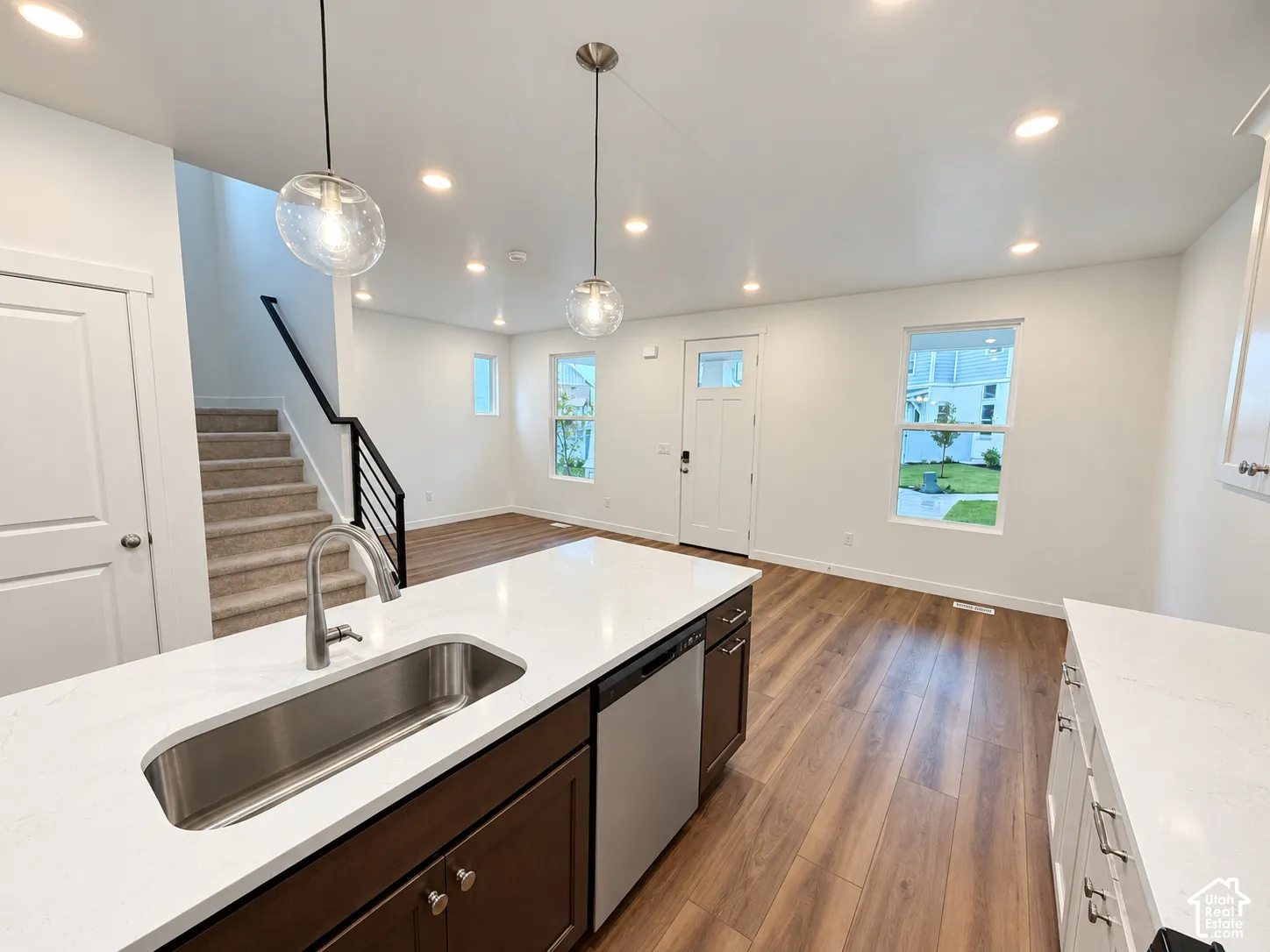 Kitchen featuring a white quartz countertop, stainless steel undermount sink, dark-finish cabinetry, wood-finish flooring, and glass pendant lighting