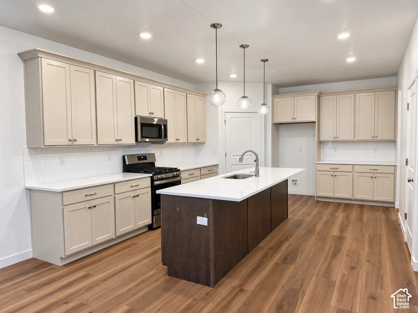 Kitchen featuring shaker-style cabinetry, quartz countertops, central island with stainless steel sink, wood-finish flooring, and recessed pendant lighting