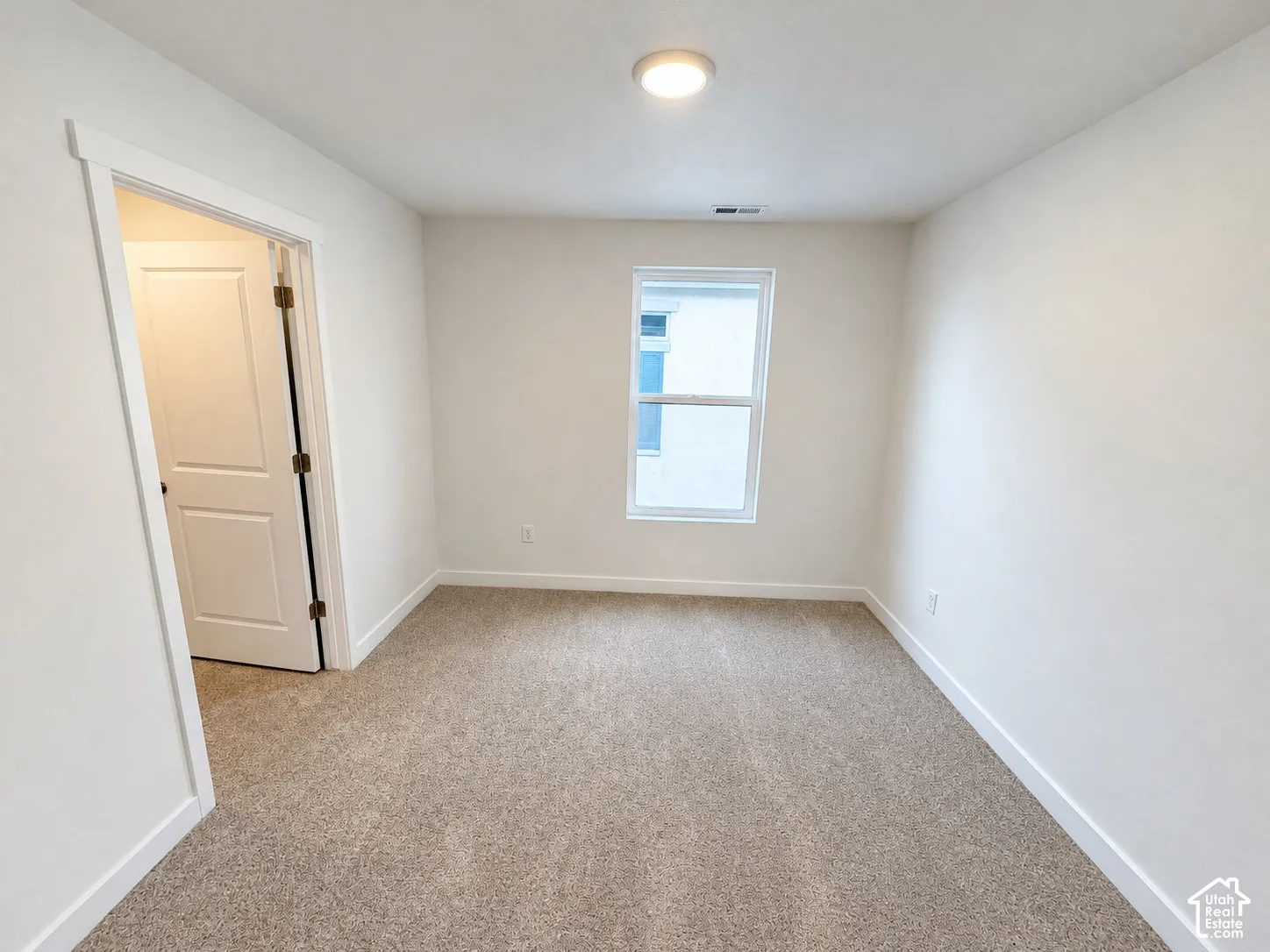 Neutral-toned carpeted flooring, white wall finishes, single-pane window, and interior door with brushed metal hardware