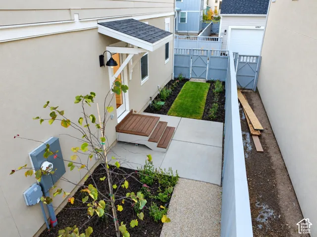 Exterior side yard featuring a concrete patio, wood-finish stairs, a covered entryway, and enclosed privacy fencing