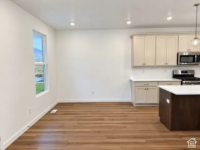 Kitchen featuring cream-colored cabinetry, stainless steel appliances, quartz countertops, a dual-tone kitchen island, and wood-finish flooring