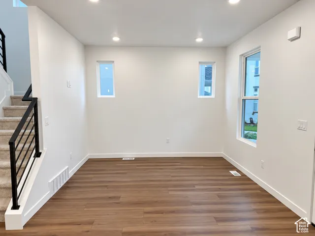 Open interior space featuring wood-finish flooring, recessed ceiling lighting, three windows, and a staircase with a black metal railing