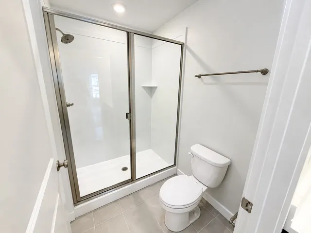 Shower enclosure with a metallic frame, integrated corner shelf, and wall-mounted showerhead, complemented by a floor-mounted toilet and ceramic tile flooring