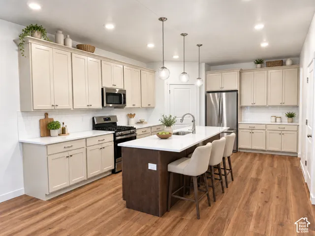 Kitchen featuring shaker-style cabinetry, white quartz countertops, subway tile backsplash, center island with a stainless steel sink, and wood-finish flooring