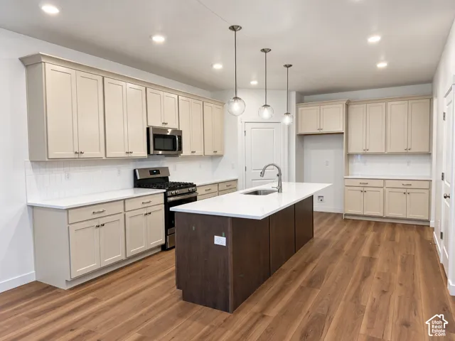 Kitchen featuring shaker-style cabinetry, quartz countertops, central island with stainless steel sink, wood-finish flooring, and recessed pendant lighting
