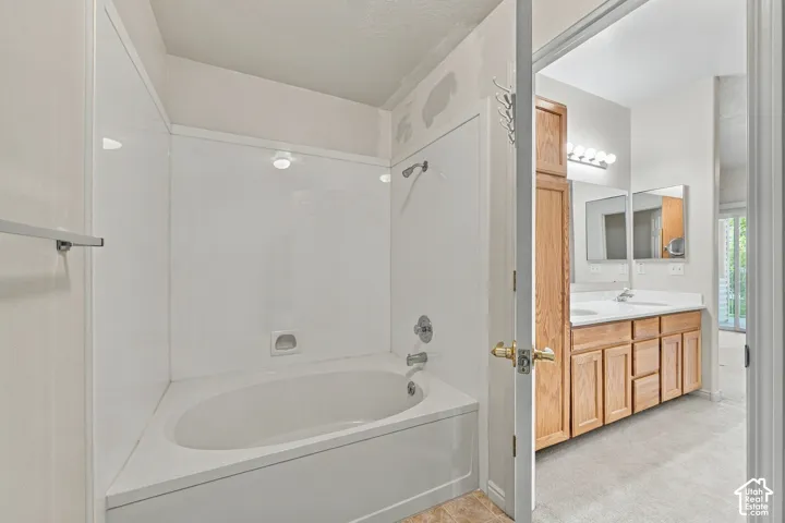Bathroom featuring a soaking tub with an integrated shower surround, wooden cabinetry, double-sink vanity, and wall-mounted vanity lighting