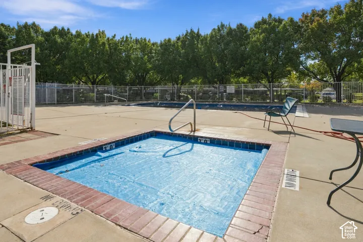 Swimming pool and spa area featuring concrete decking, metal safety fencing, and brick trim