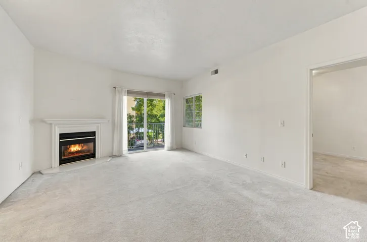 Open-concept interior featuring a fireplace with a white mantel, wall-to-wall carpeting, and a sliding glass door providing access to a balcony