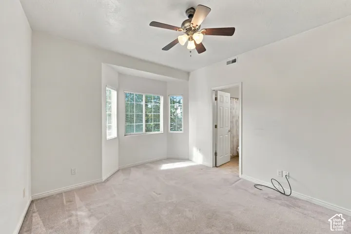 Bedroom featuring neutral wall tones, carpet flooring, a three-panel bay window, and a multi-light ceiling fan