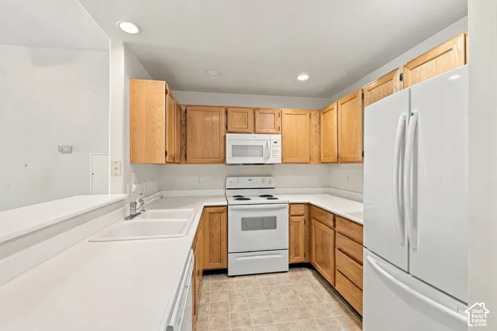 Kitchen featuring natural wood-finish cabinetry, solid-surface countertops, dual-basin sink, and white appliances including a built-in microwave and refrigerator