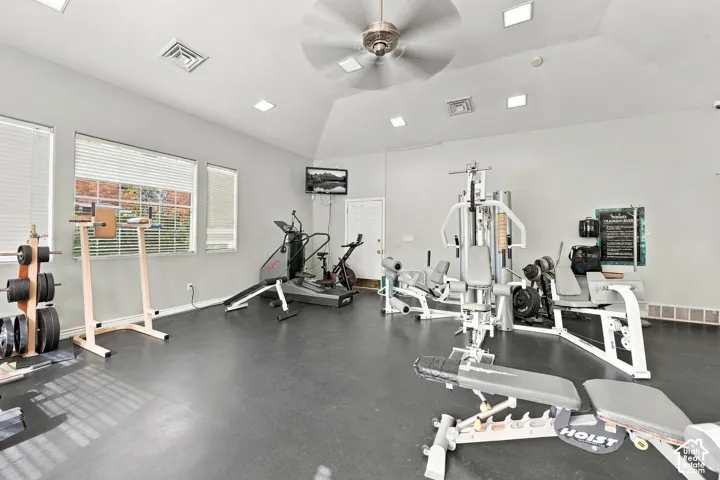 Vaulted ceiling with recessed lighting and a central ceiling fan, expansive rubberized flooring, and oversized windows providing natural light