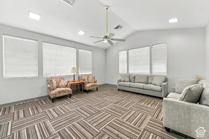 Vaulted ceilings, recessed lighting, patterned carpet tile flooring, and multiple windows with horizontal blinds