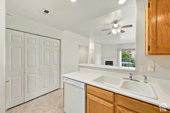 Kitchen area featuring solid-surface countertops, dual-basin sink with metallic faucet, white dishwasher, wooden cabinetry, and bifold closet doors