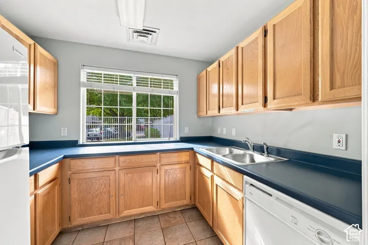 Kitchen featuring light wood cabinetry, expansive solid-surface countertops, dual-basin stainless steel sink, tile flooring, and large window with muntin detailing