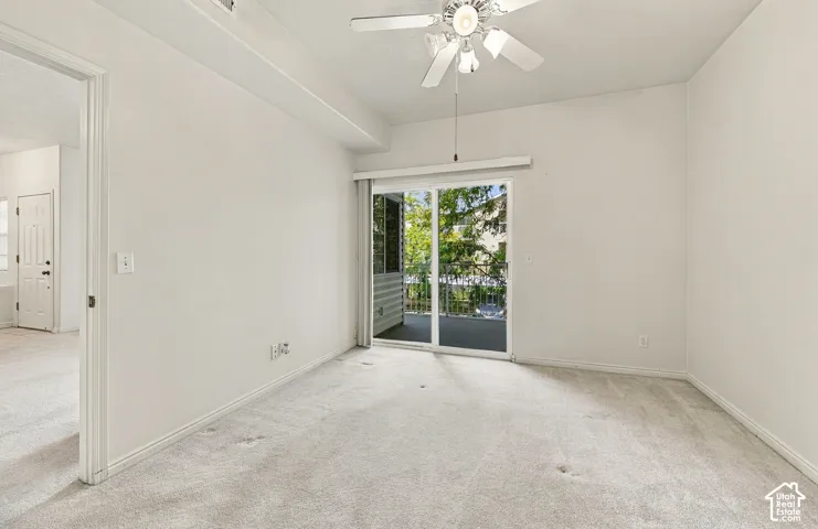 Primary bedroom featuring neutral carpeting, a ceiling fan with light fixture, and a sliding glass door providing external access to a balcony with a metal railing
