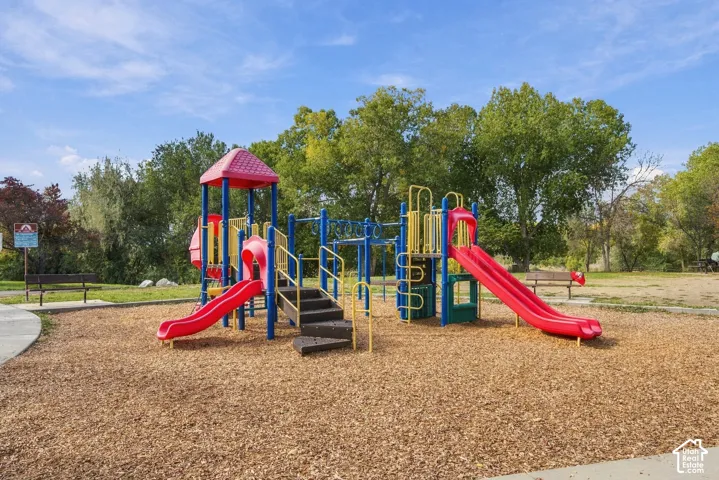 Outdoor recreation area featuring a multi-level composite playground structure with slides, climbing components, wood chip surfacing, and park benches