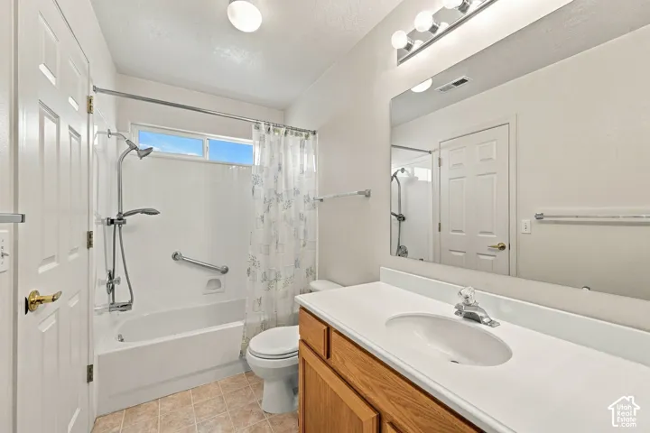 Full bathroom featuring a wood-finish vanity with a white countertop, oval basin sink, large wall-mounted mirror, and a shower-tub combination with a wall-mounted grab bar