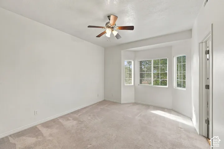 Bedroom featuring neutral carpeting, a multi-pane bay window, and a ceiling fan with integrated lighting