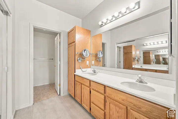 Dual-sink vanity with wood-finish cabinetry, solid surface countertop, wall-to-wall mirror, and integrated lighting