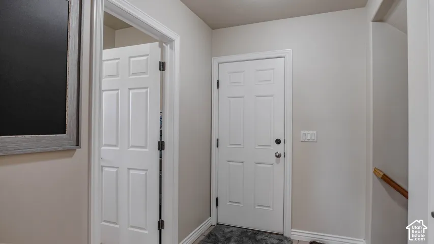 Neutral-toned entryway featuring a six-panel exterior door, matching interior doors, and a staircase with a wooden handrail