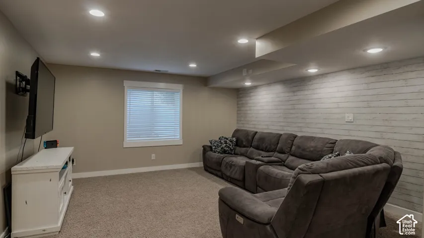 Recessed lighting, wall-mounted television bracket, neutral carpeting, and horizontal plank accent wall