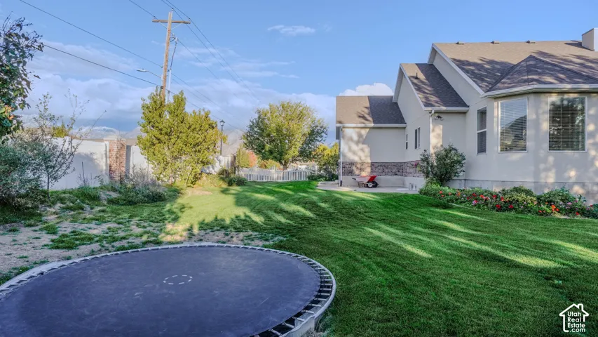 Backyard featuring a manicured lawn, stone veneer foundation accents, and vinyl perimeter fencing