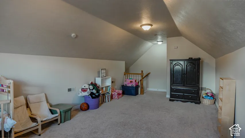 Finished attic space featuring vaulted ceilings, neutral wall tones, wall-to-wall carpeting, and a wooden stair railing with white balusters