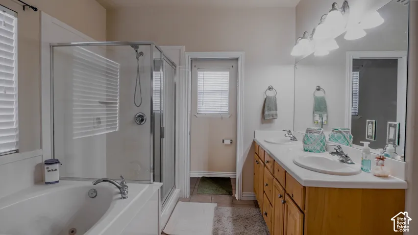 Bathroom featuring a dual-sink vanity with light wood cabinetry, a deep soaking tub, and a separate glass-enclosed shower