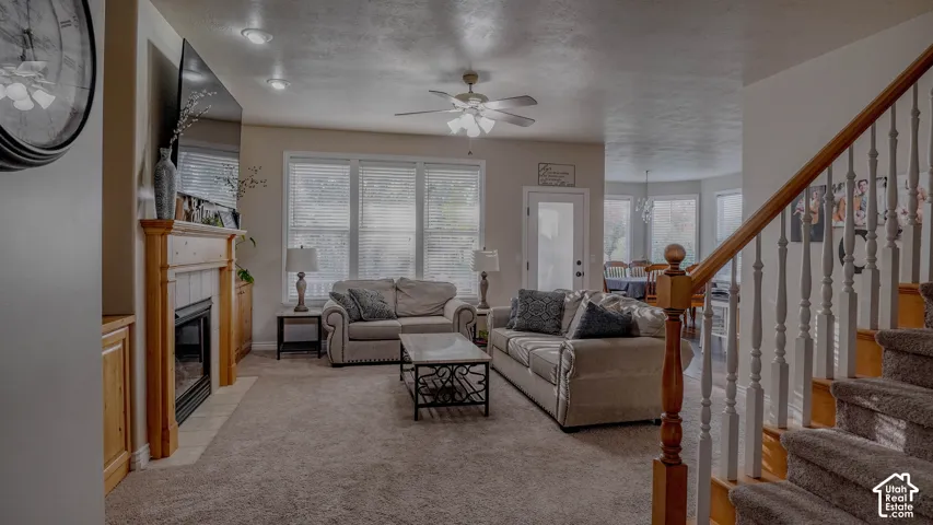 Living area featuring a fireplace with a wood mantel, built-in cabinetry, carpeted flooring, a ceiling fan with integrated lighting, and a staircase with a wooden handrail and white balusters