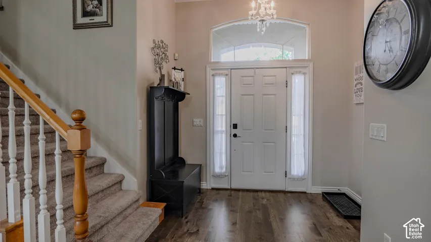 Entryway featuring wood-finish flooring, a white front door with flanking sidelights, an arched transom window, a staircase with a wooden banister, and a hanging chandelier