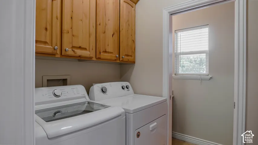 Laundry area featuring wood-finish wall-mounted cabinetry, a window with horizontal blinds, and dedicated hookups